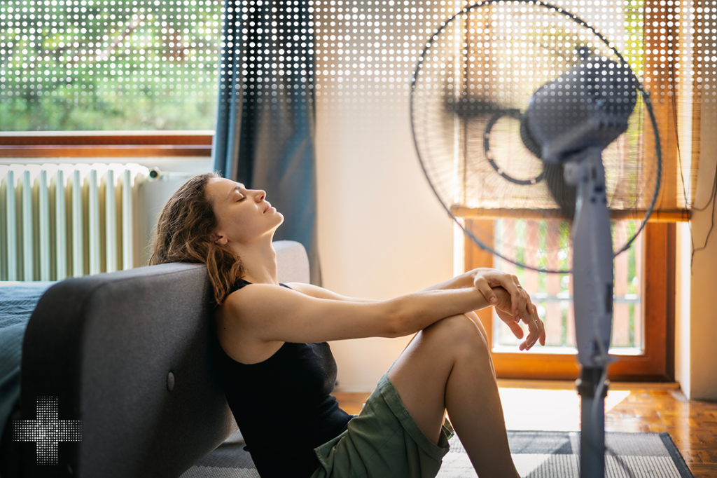 Young woman sitting at home on the floor in front of a fan saving from heat