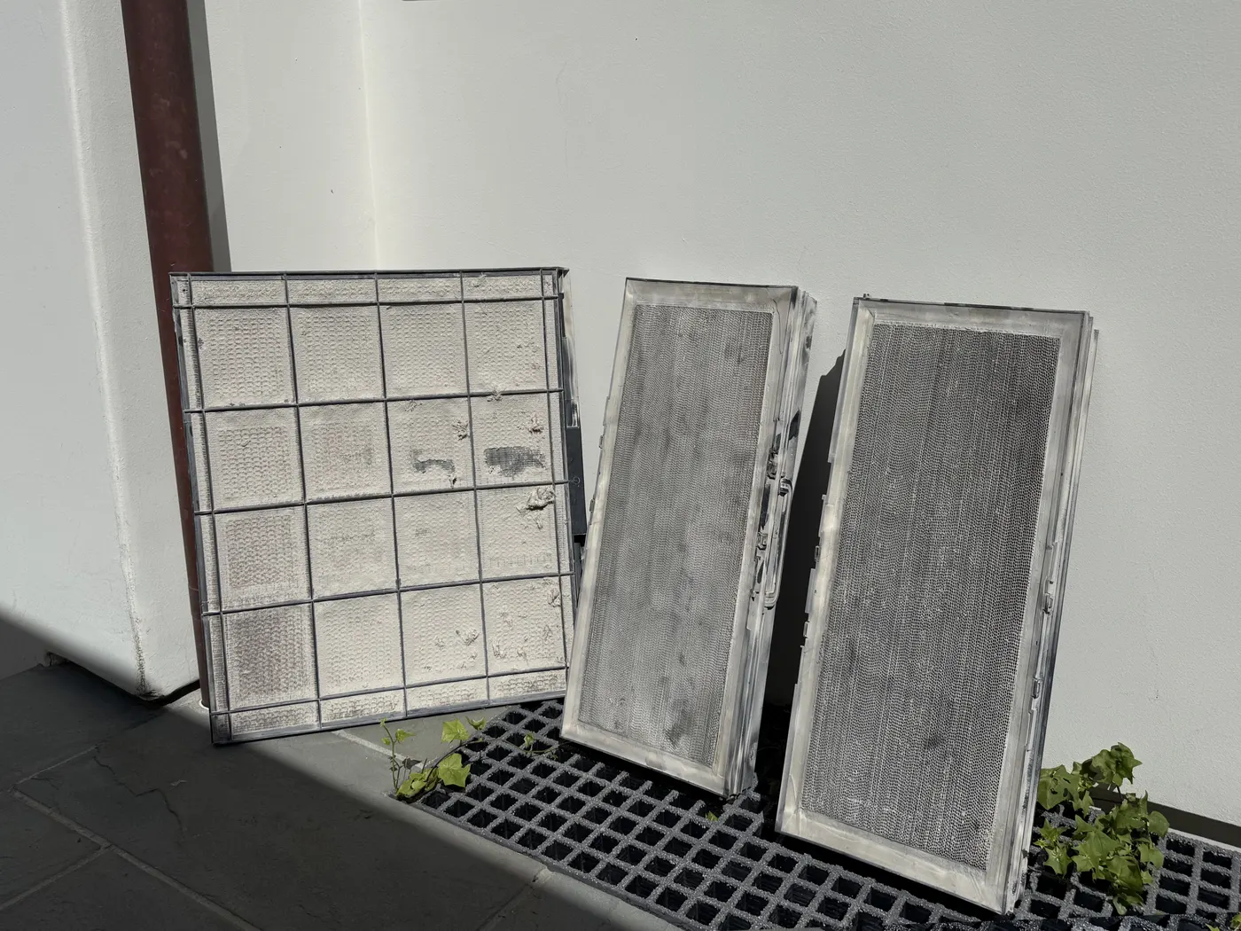 Three air filters leaning against a wall, covered in dust and lint.