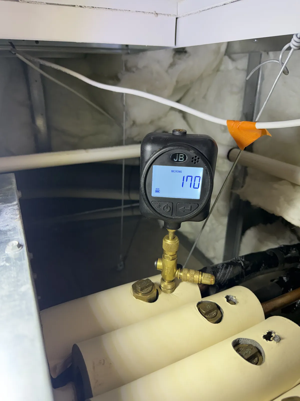 Digital gauge connected to a valve beside insulated refrigerant lines.