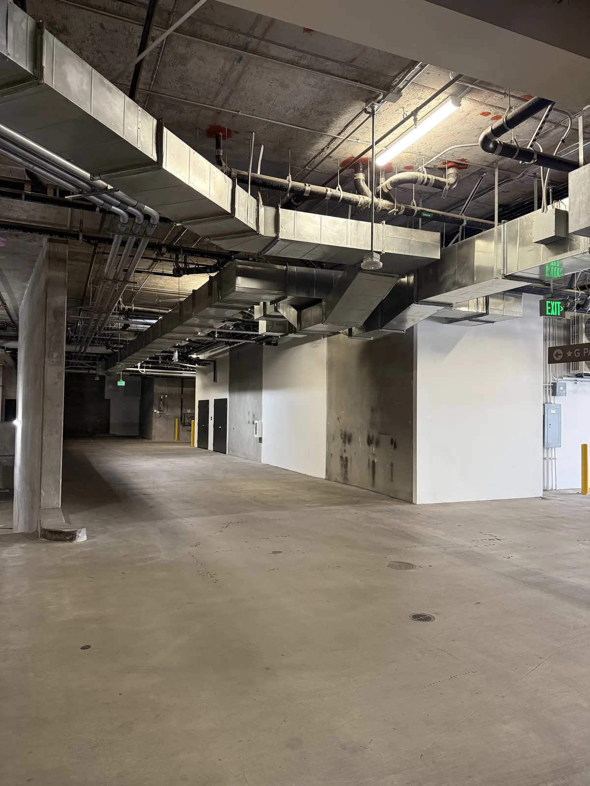 Large rectangular ducts and pipes along the ceiling of an underground parking garage.
