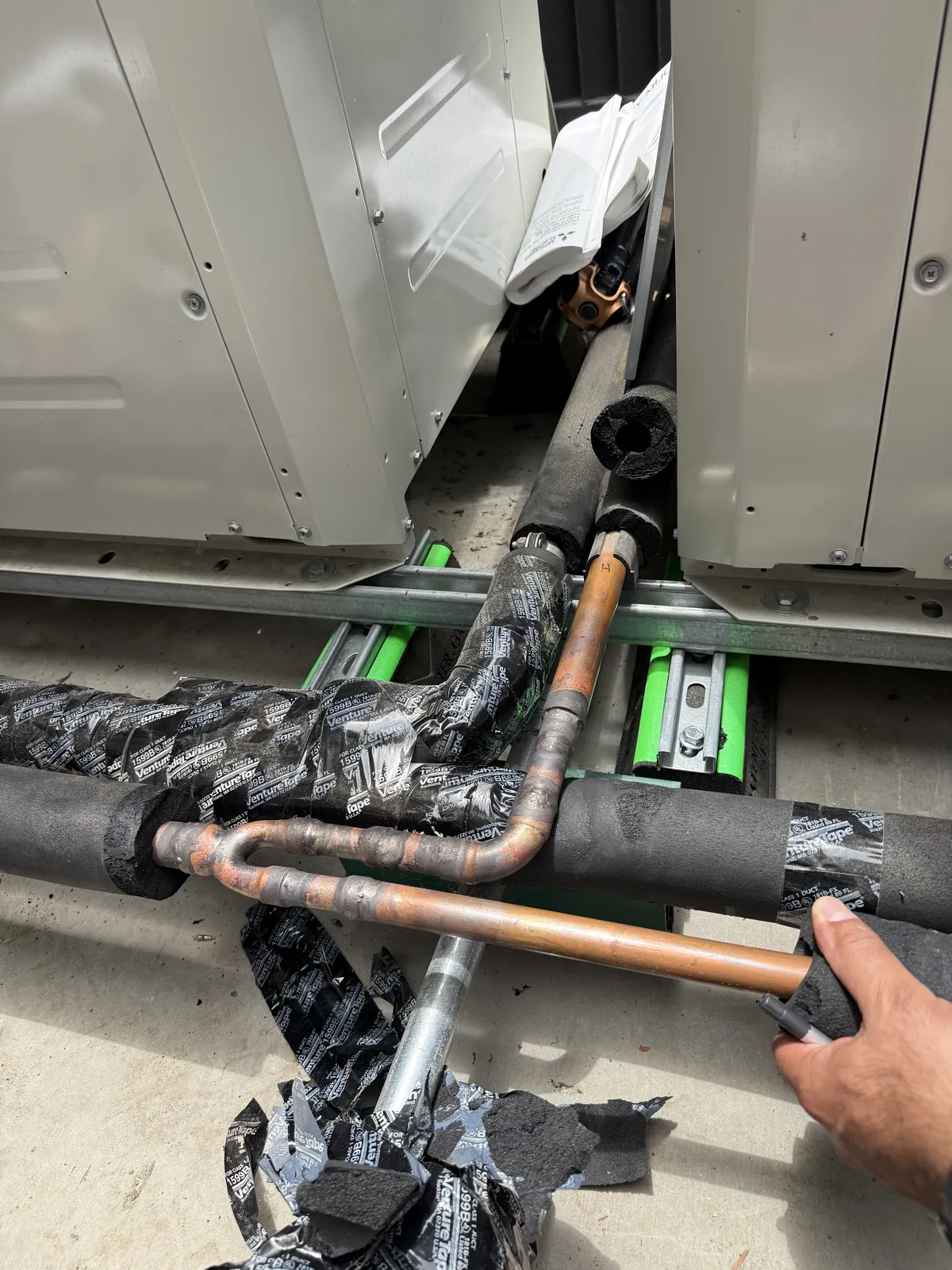 A hand at refrigerant piping and valves beside an outdoor unit.