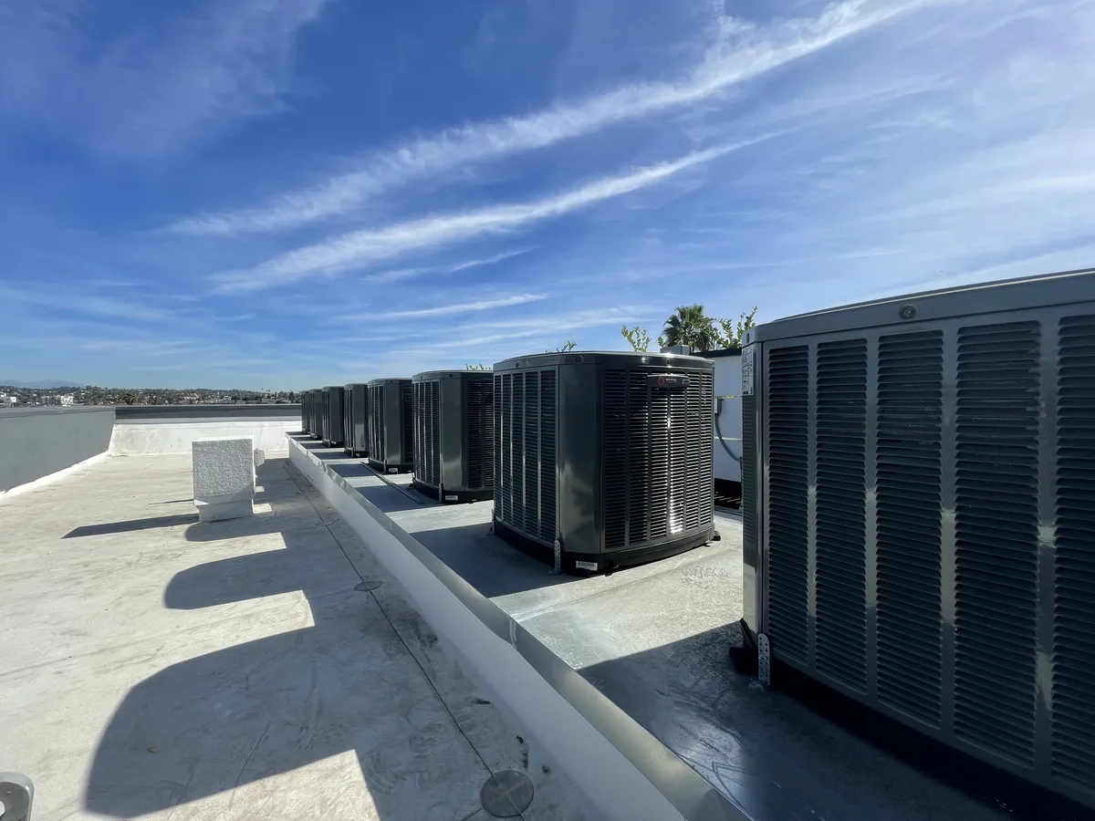 Outdoor units lined up along a rooftop parapet under a blue sky with thin clouds.