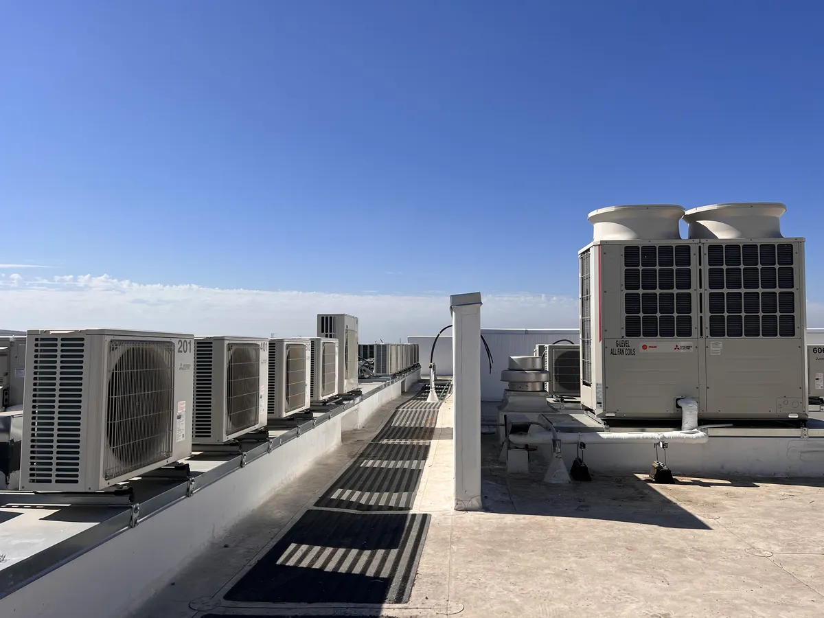 Row of outdoor units along a rooftop edge with a larger unit at the far end, under a clear blue sky.