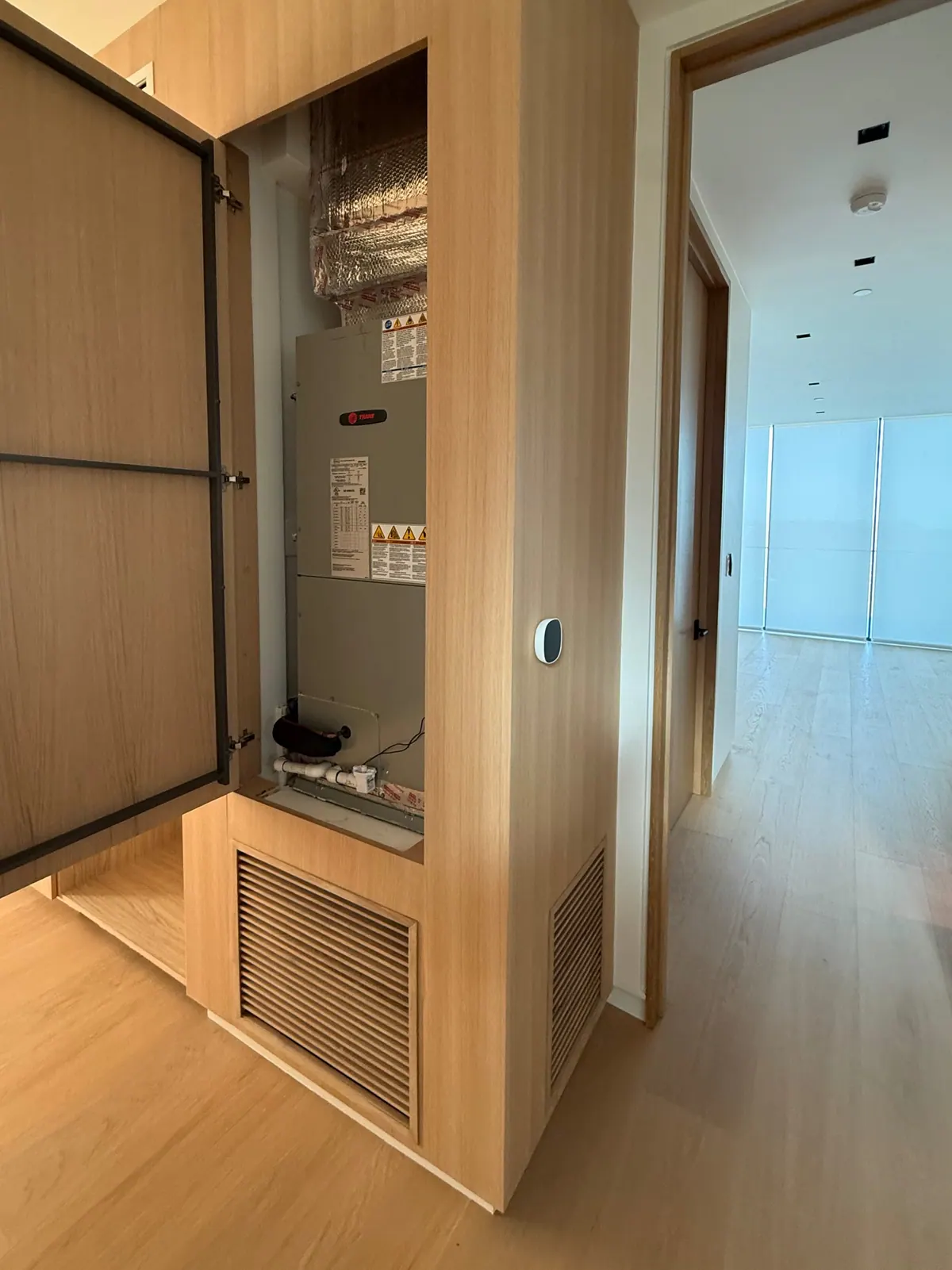 Access door open on equipment built into an oak wall, with a louvered grille below.