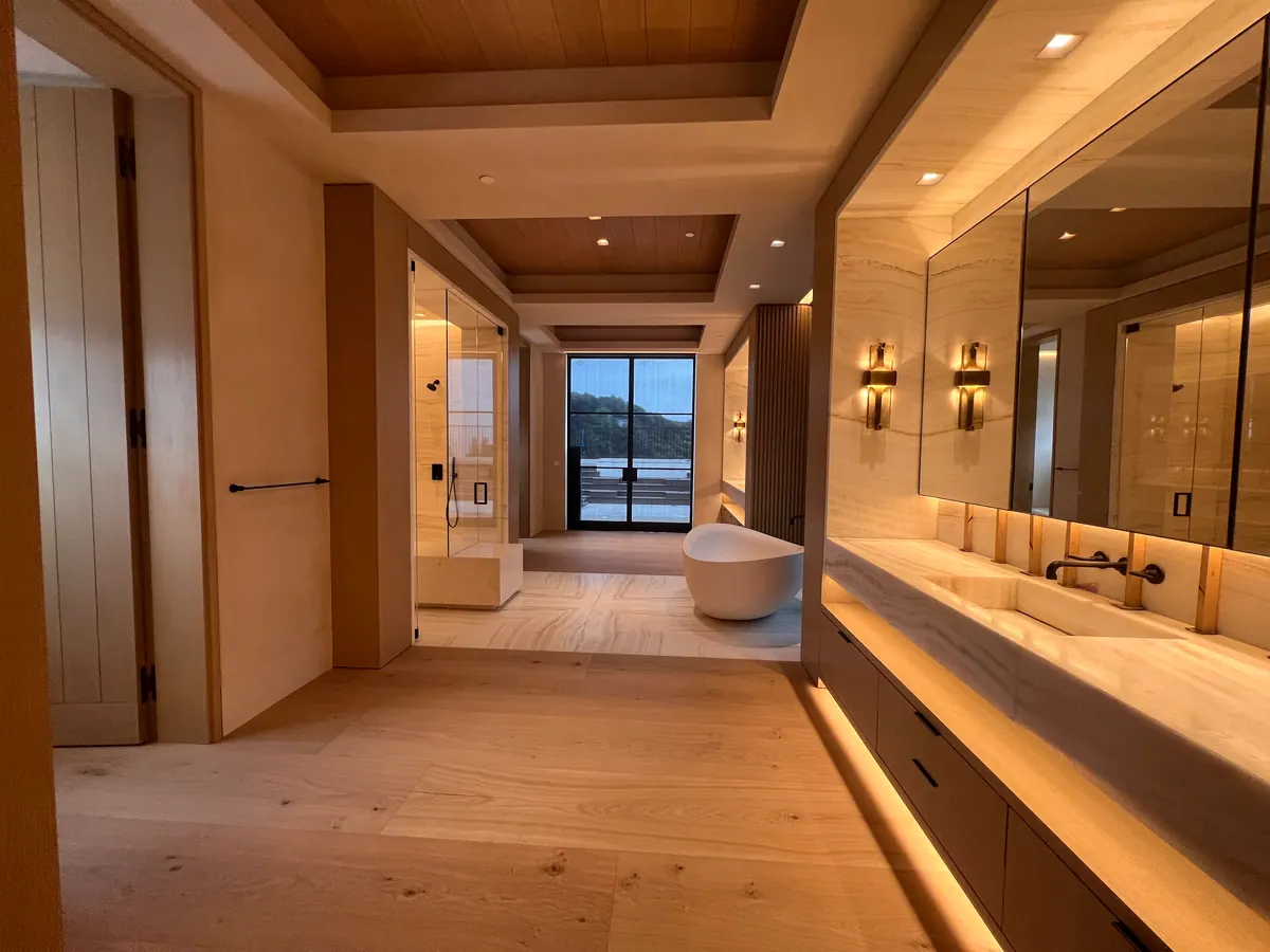 Long bathroom with a floating oak vanity, a freestanding tub, and a window at the far end.