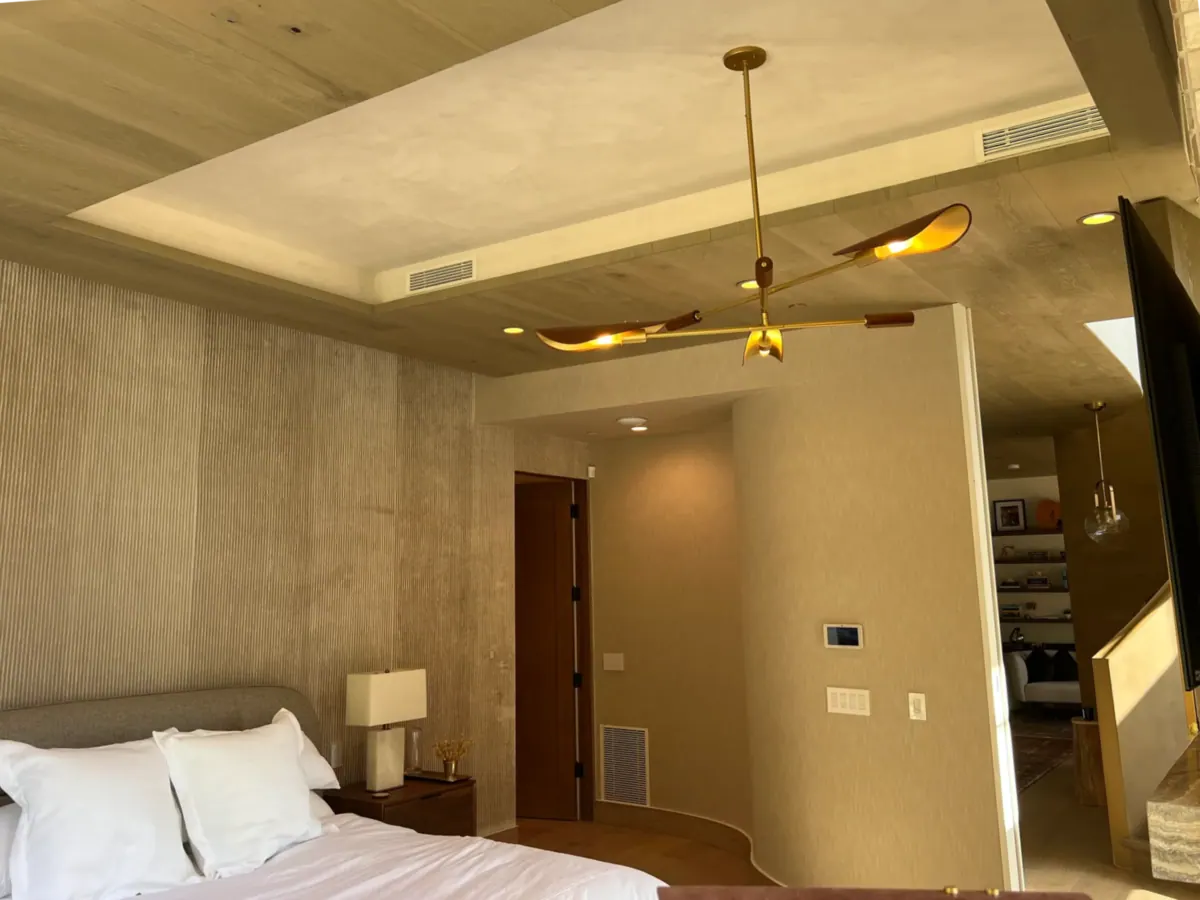 Bedroom with a tray ceiling, a ceiling fan, and a textured wall behind the bed.