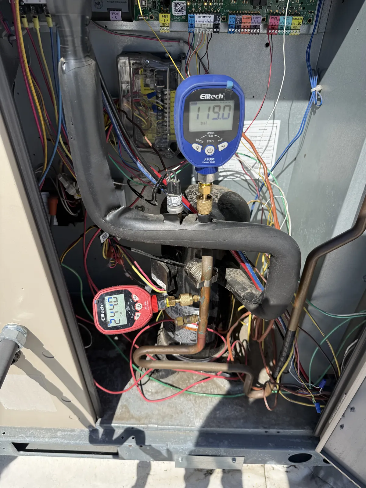 Two digital pressure gauges connected to a compressor inside an open outdoor unit.