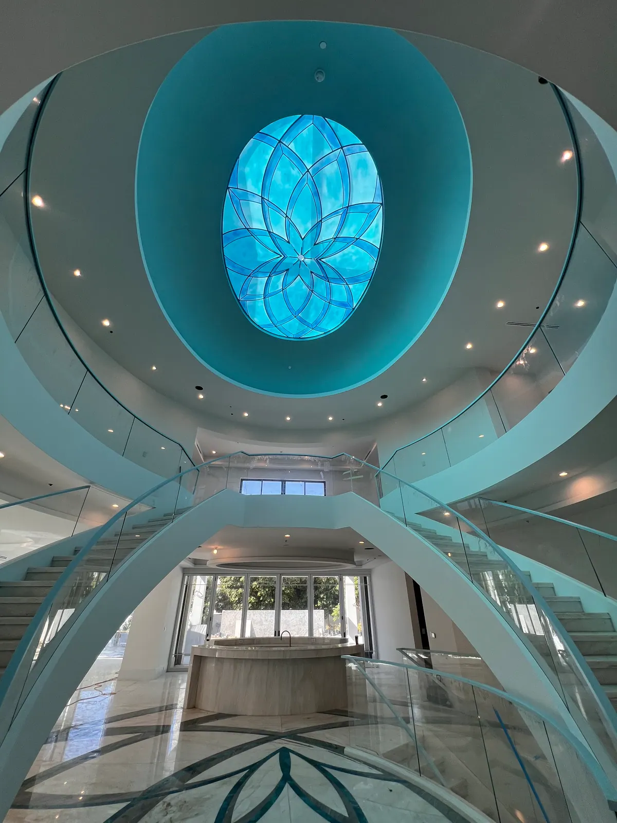 Looking up past two curved glass staircases to an oval blue glass skylight.