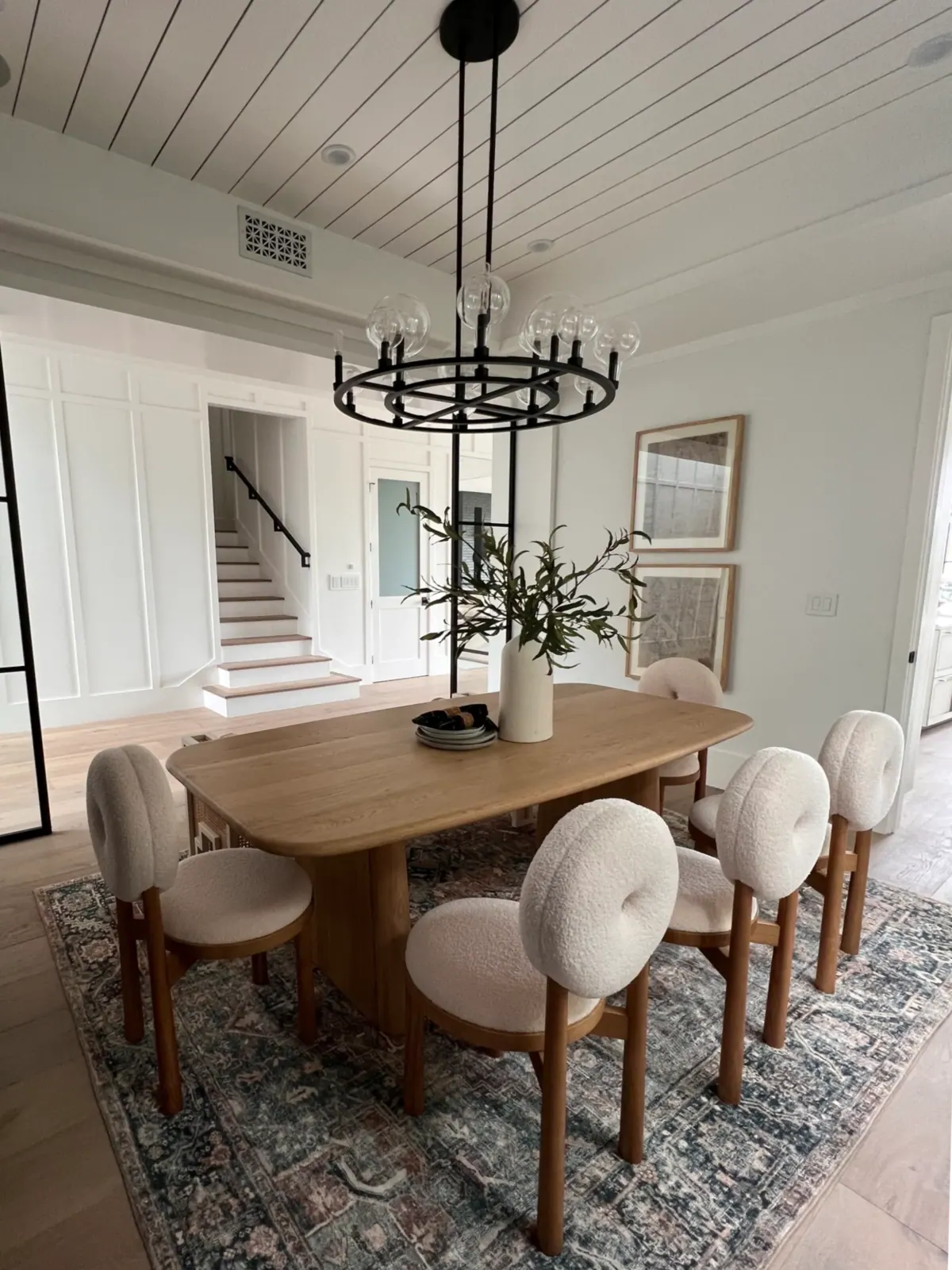 Dining room with an oval oak table, round upholstered chairs, a chandelier, and a white plank ceiling.