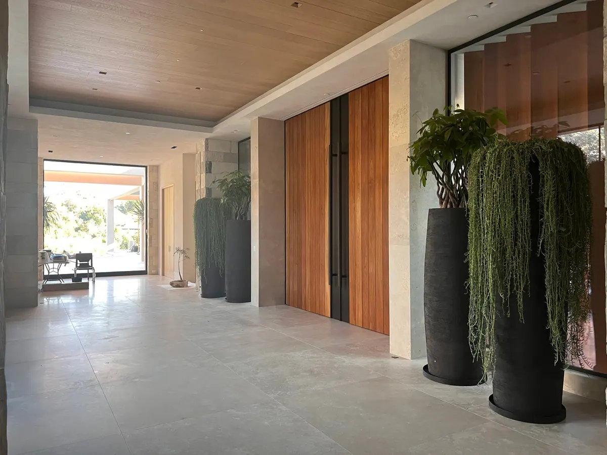 Wide hall with stone flooring, a wood-paneled wall, and two tall black planters.