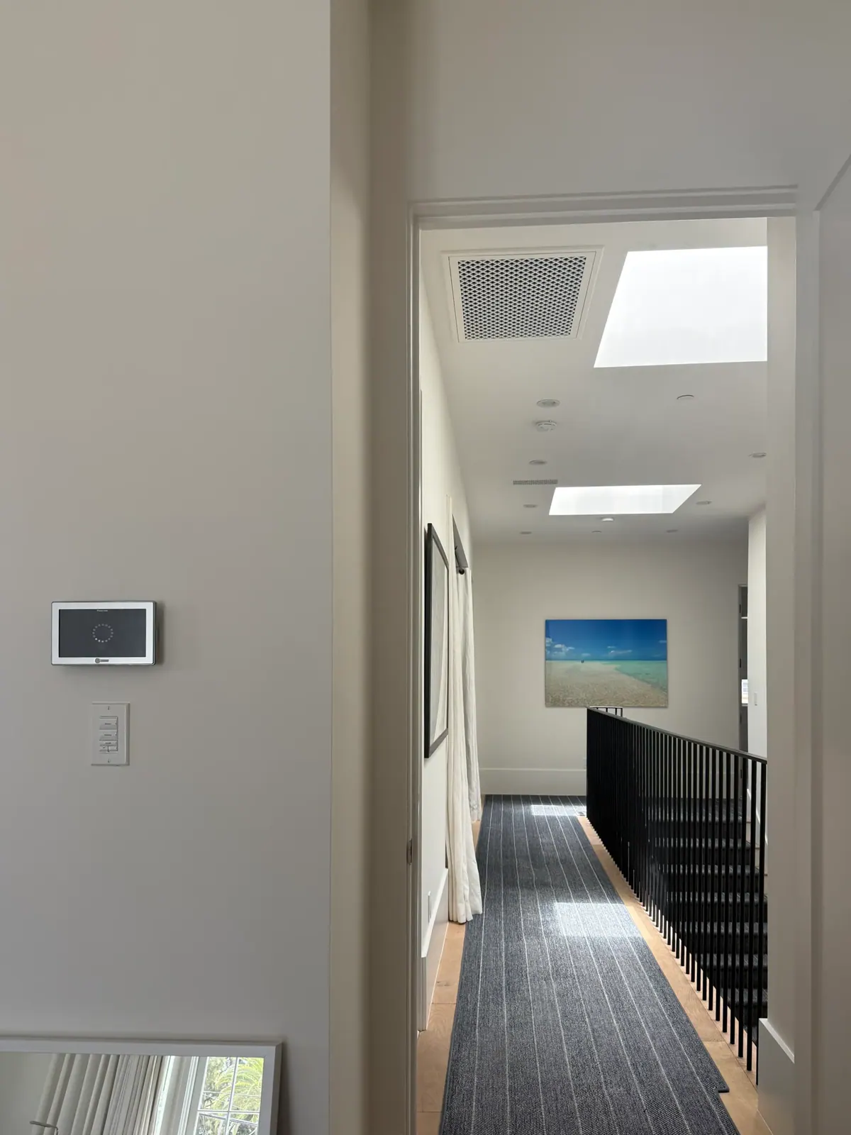 Hallway with a wall thermostat, two skylights, and a dark stair runner.