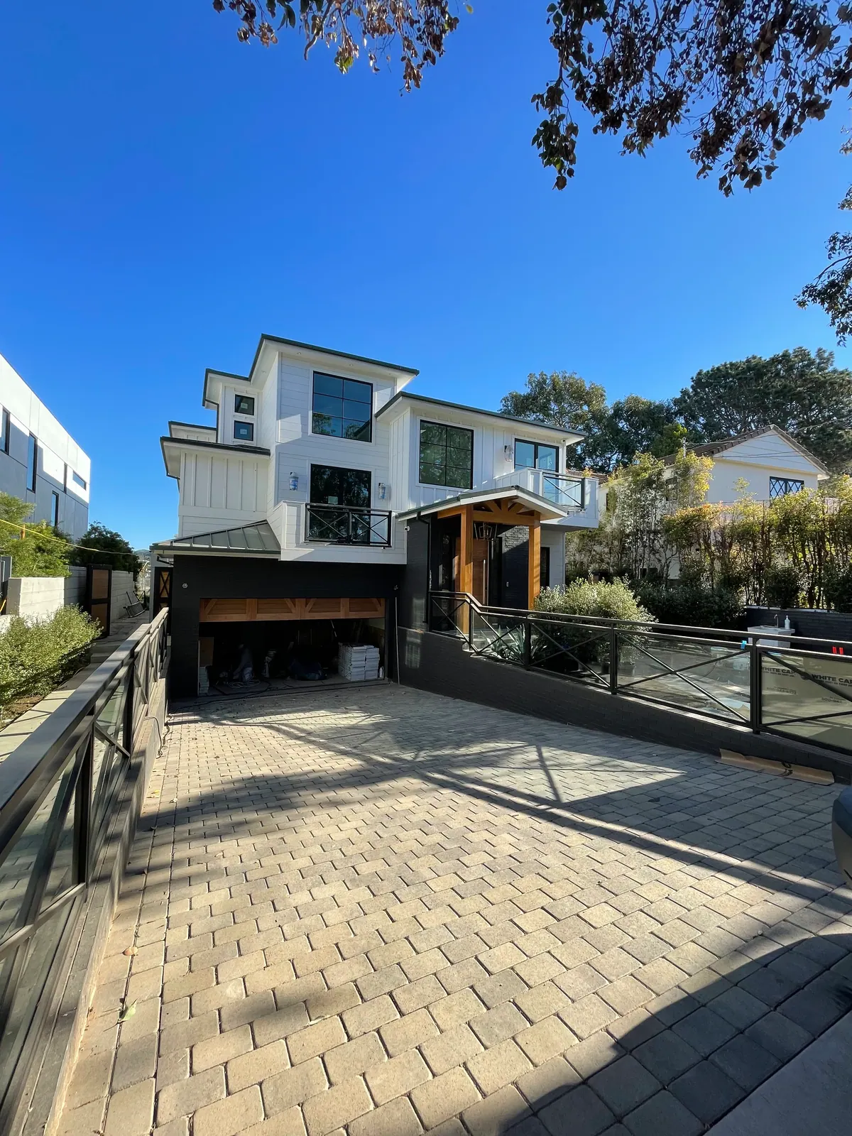 White home with a paver driveway and a glass railing.
