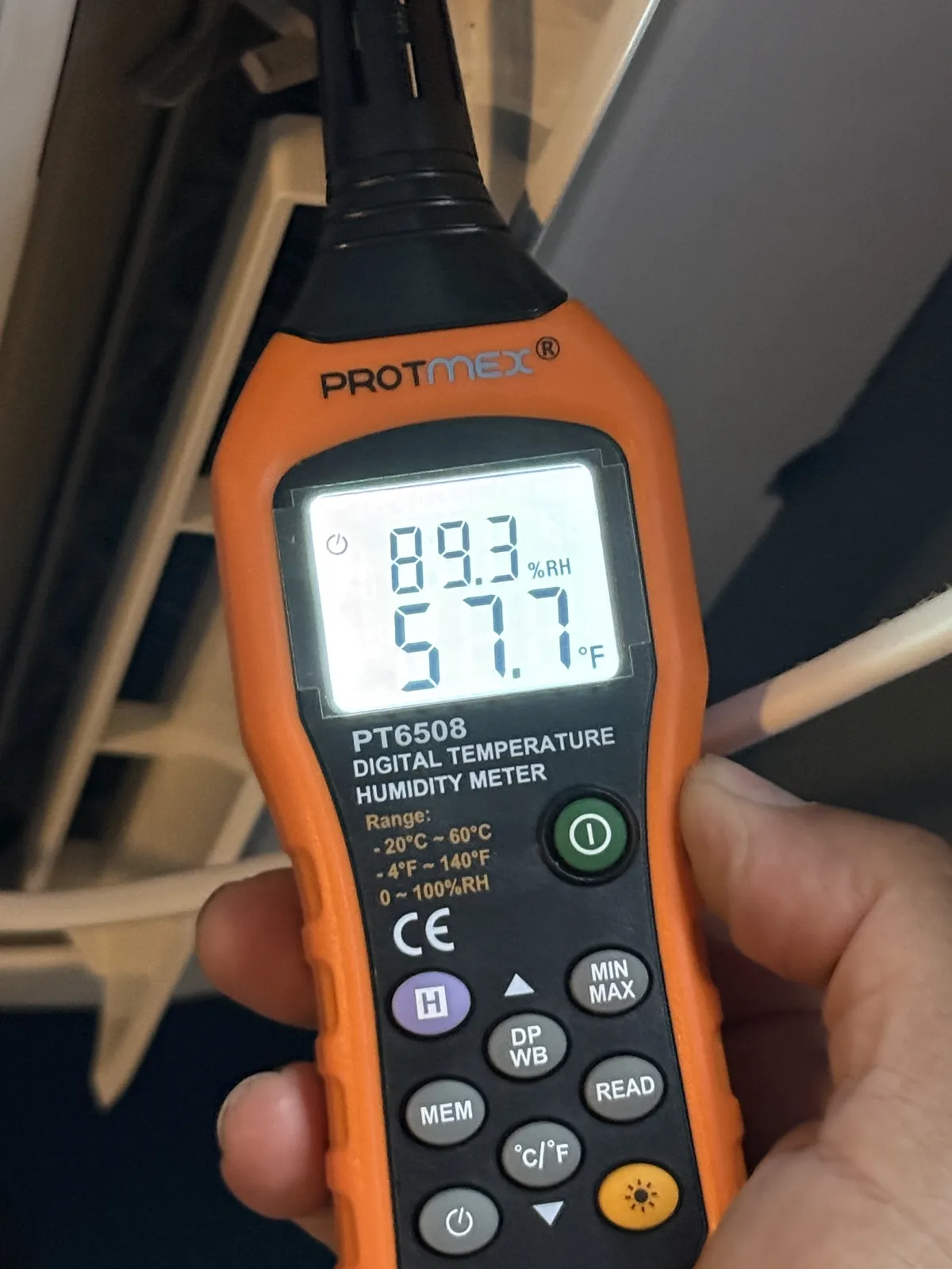 Hand-held digital meter reading 57.7°F and 89.3% humidity.