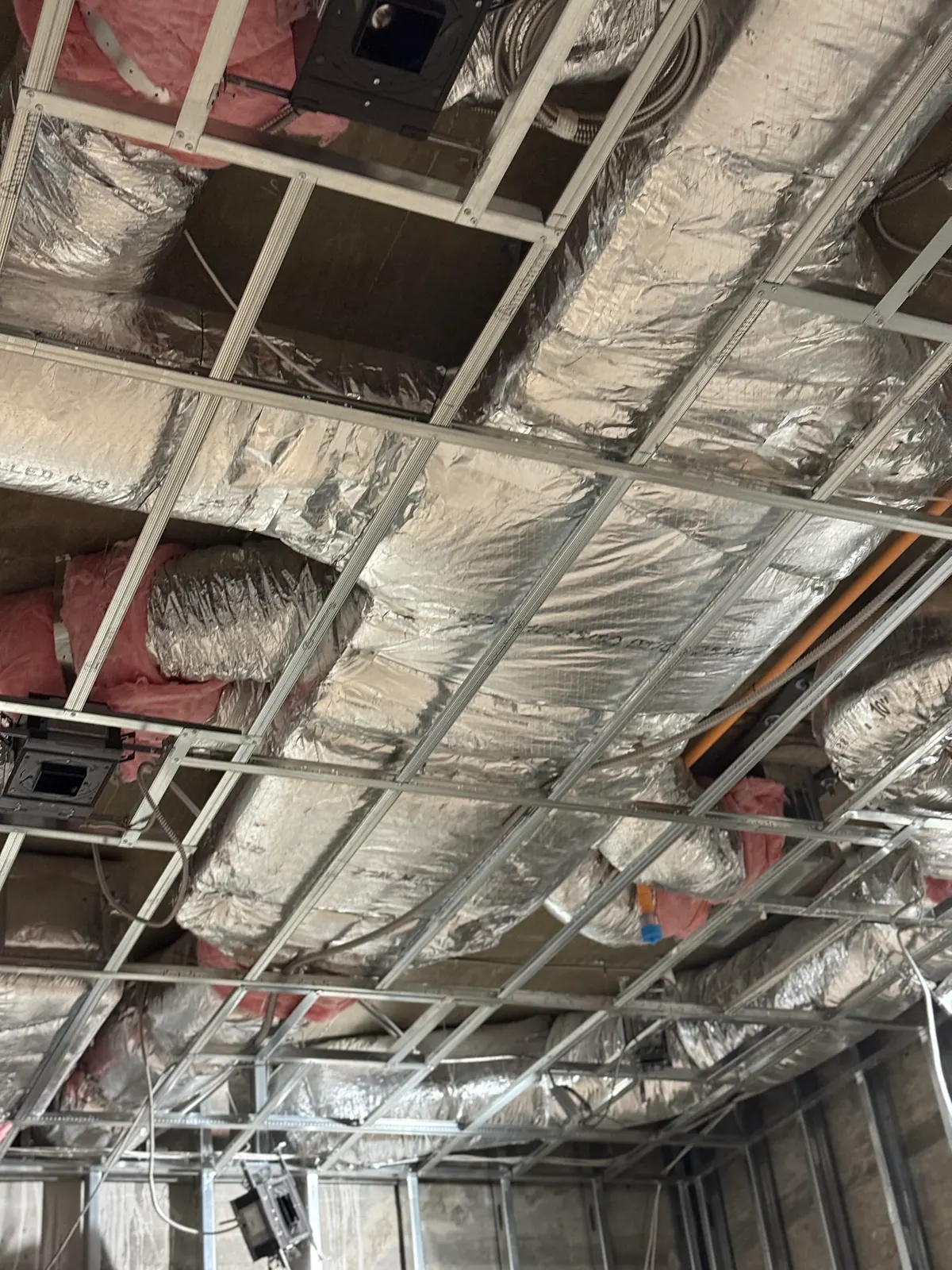 Looking up at insulated ductwork above metal ceiling framing.
