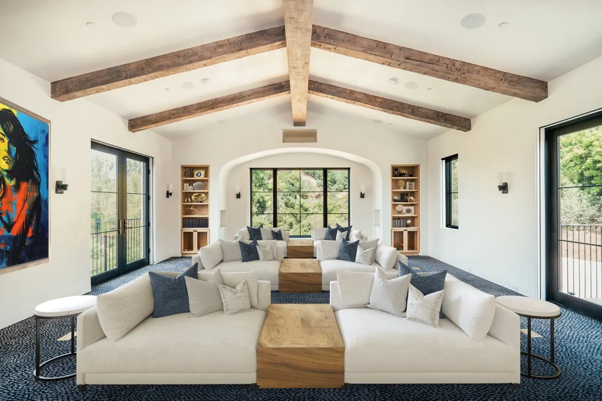 Living room with exposed wood beams, tall black-framed doors, and a large white sectional sofa.