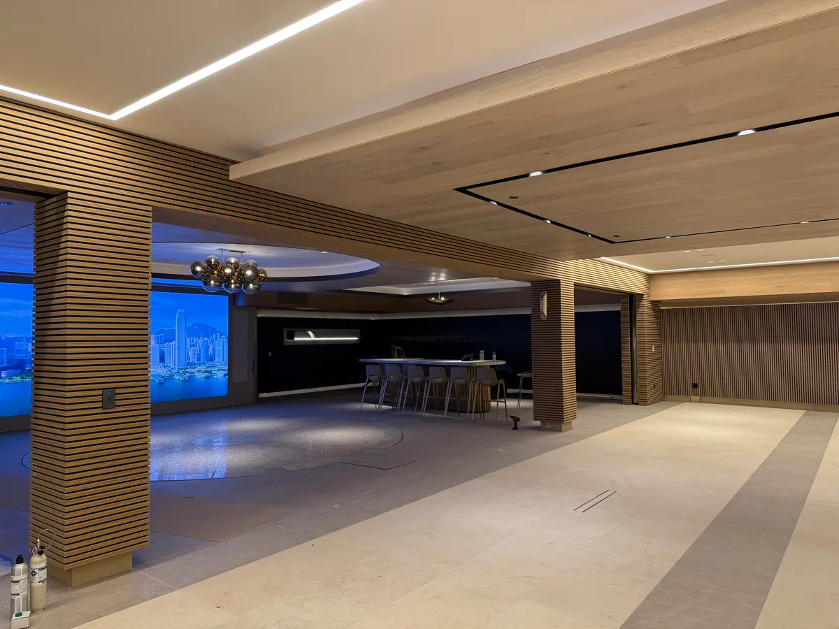 Large lounge with wood-slat columns, a lit ceiling, and a bar in the distance.
