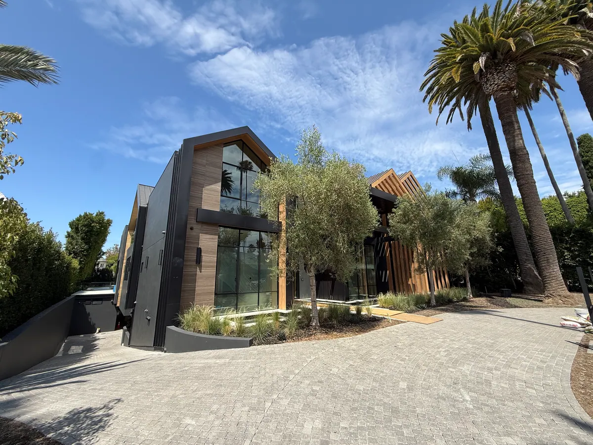 Modern home with wood and dark cladding, olive trees, and a paver driveway.