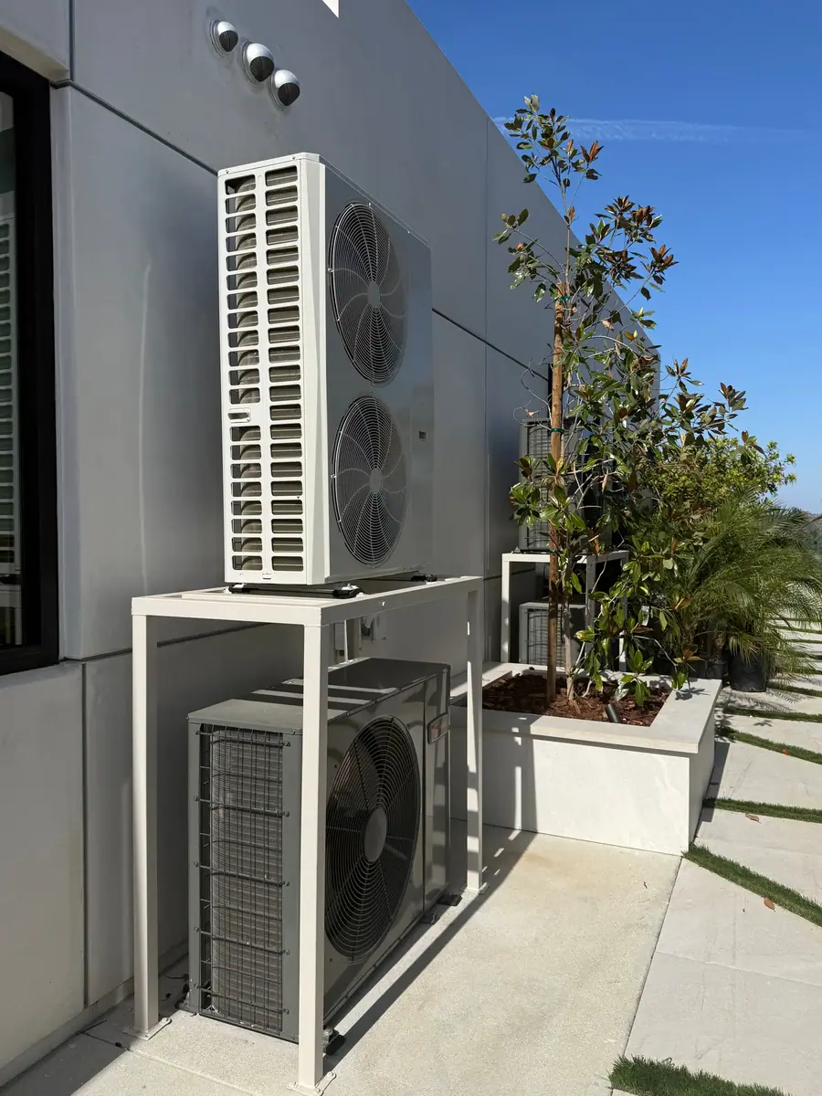 Two outdoor units mounted on a steel frame against the wall of a modern home.