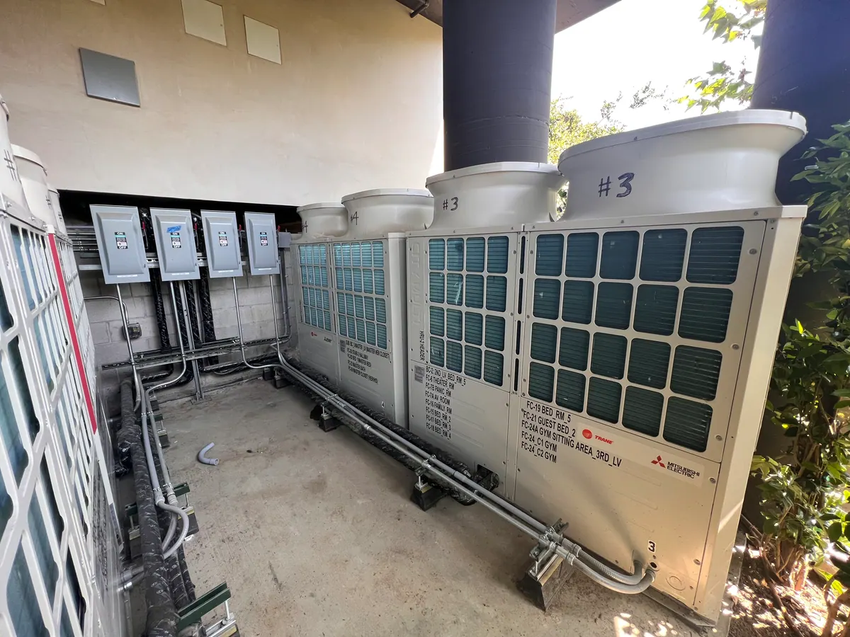 Row of outdoor units in a service alcove with piping along the wall.