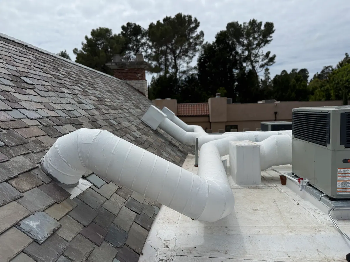 Rooftop unit with white ductwork beside a sloped tile roof.