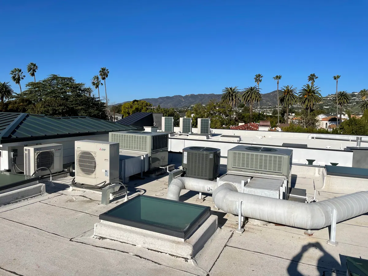 Rooftop units and white ductwork beside a skylight on a flat roof.
