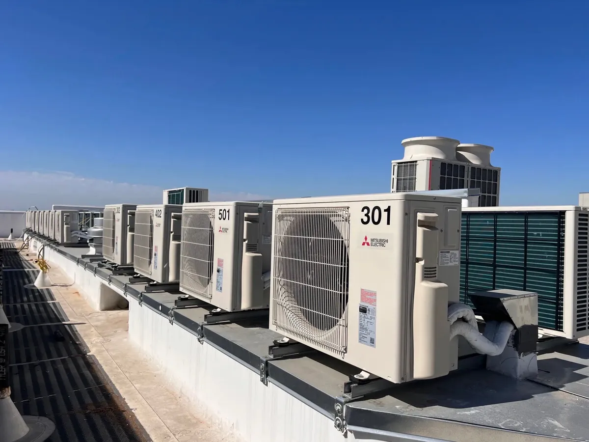 Row of outdoor units along a rooftop parapet under a blue sky.