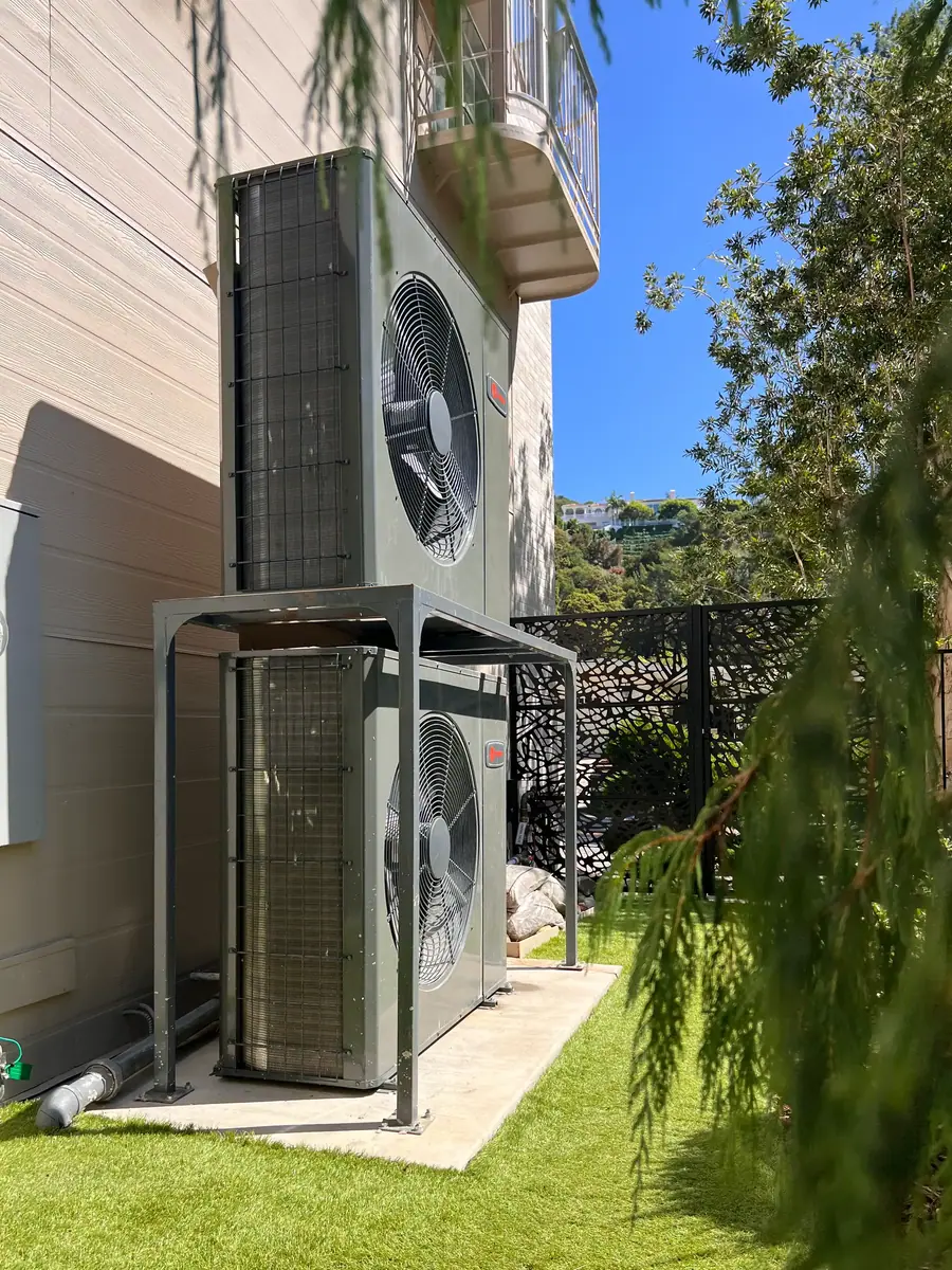 Two outdoor units stacked on a steel frame beside a home.