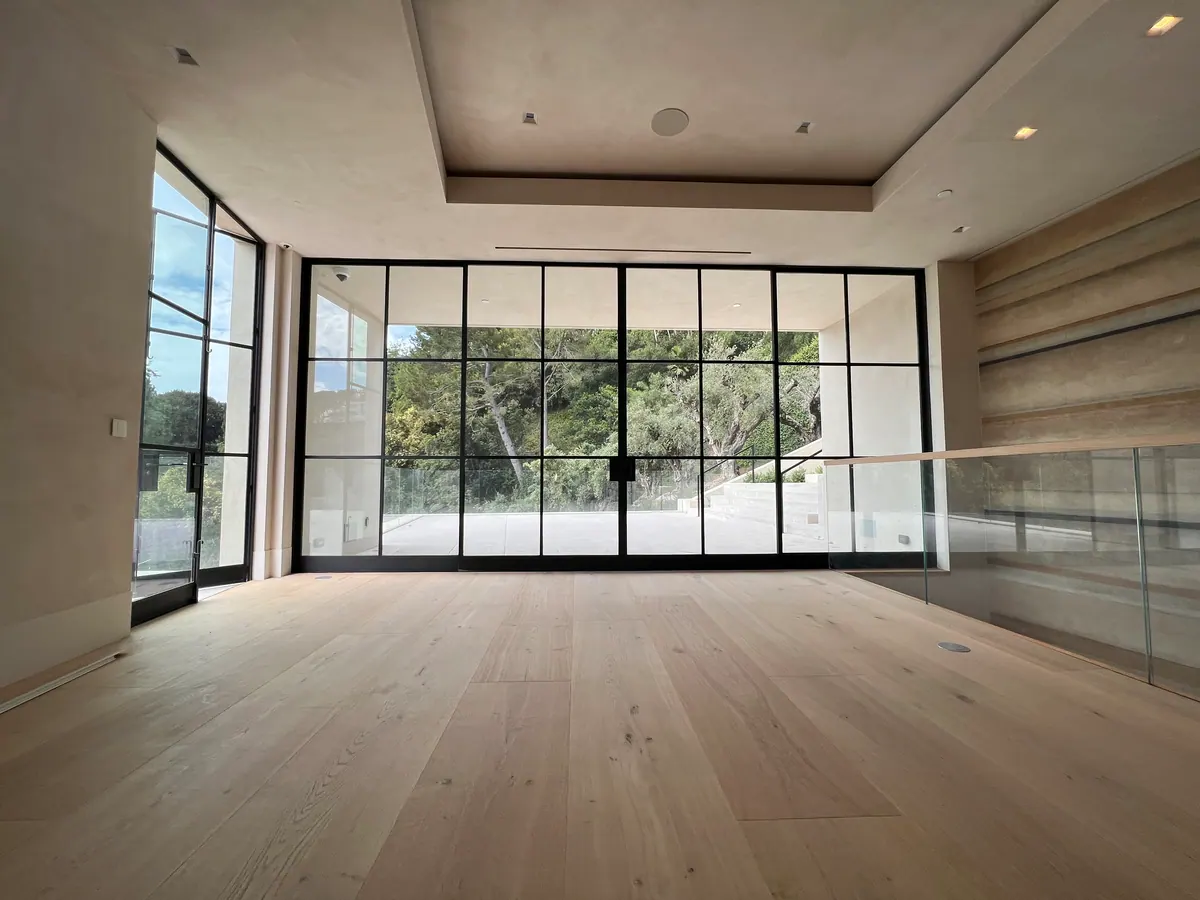 Room with black steel-framed windows, wide oak flooring, and a glass railing.