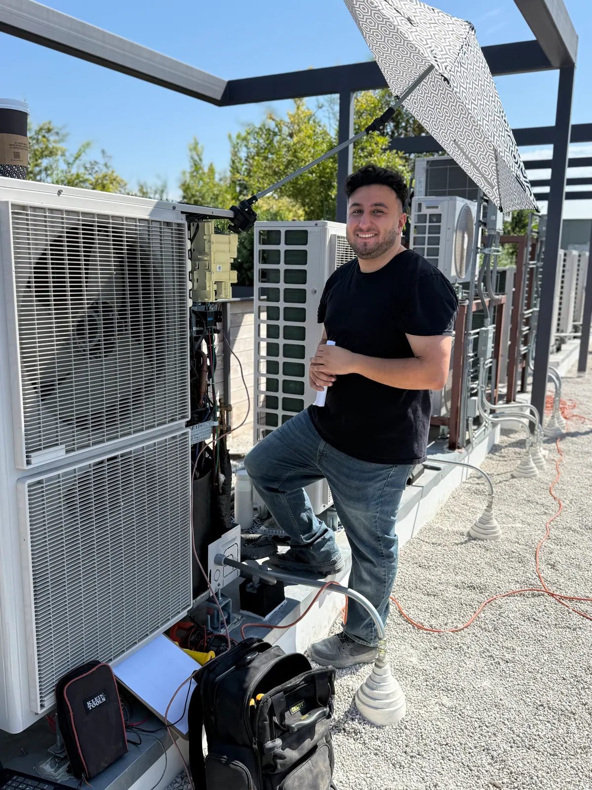 Air Plus HVAC technician standing beside outdoor units on a rooftop.