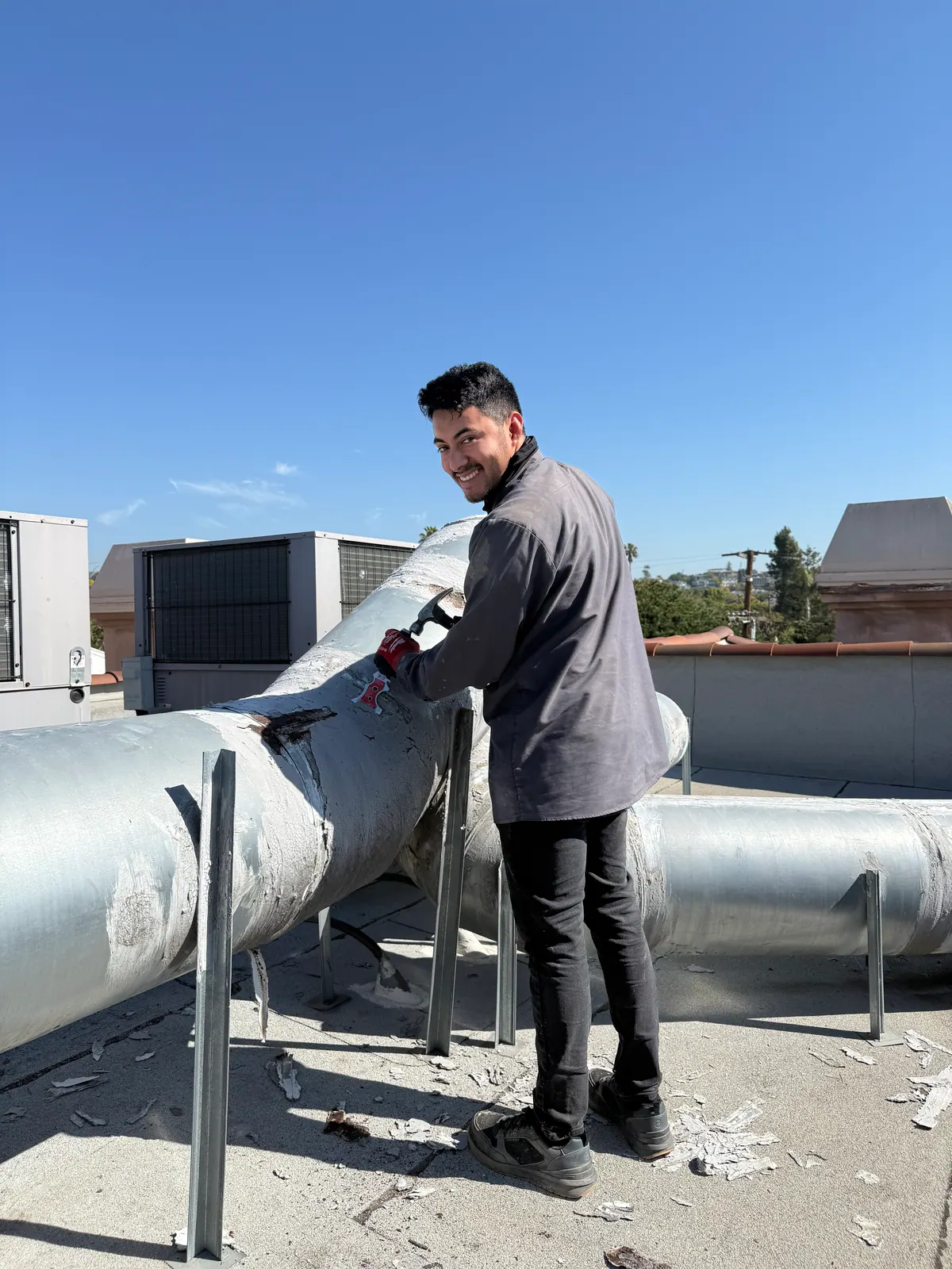 Air Plus HVAC technician on a rooftop beside large insulated ductwork.