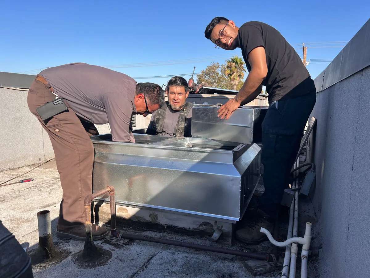 Air Plus HVAC technicians bending over a sheet metal duct section on a roof.