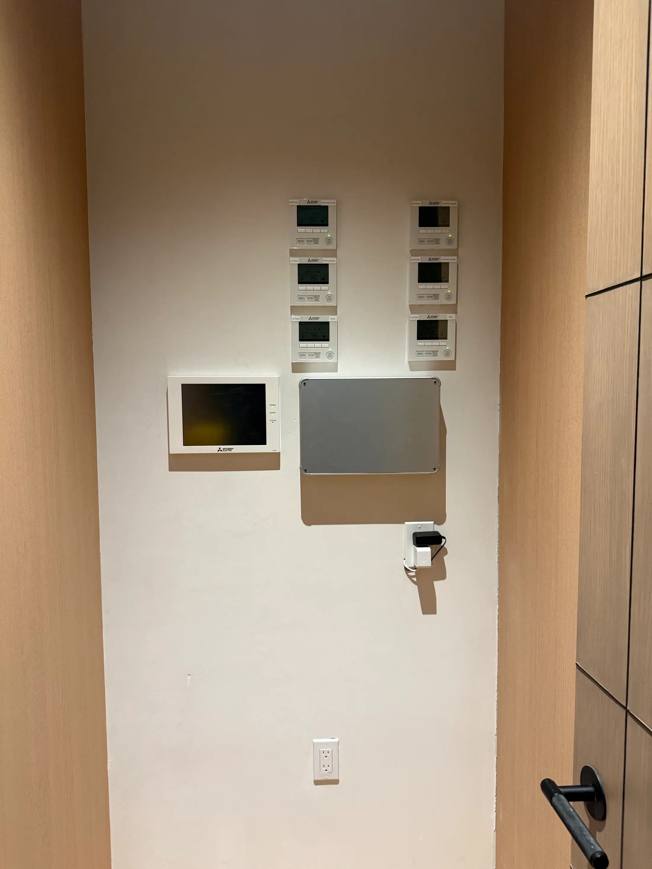 Wall controls and a touchscreen panel on a white wall beside oak paneling.