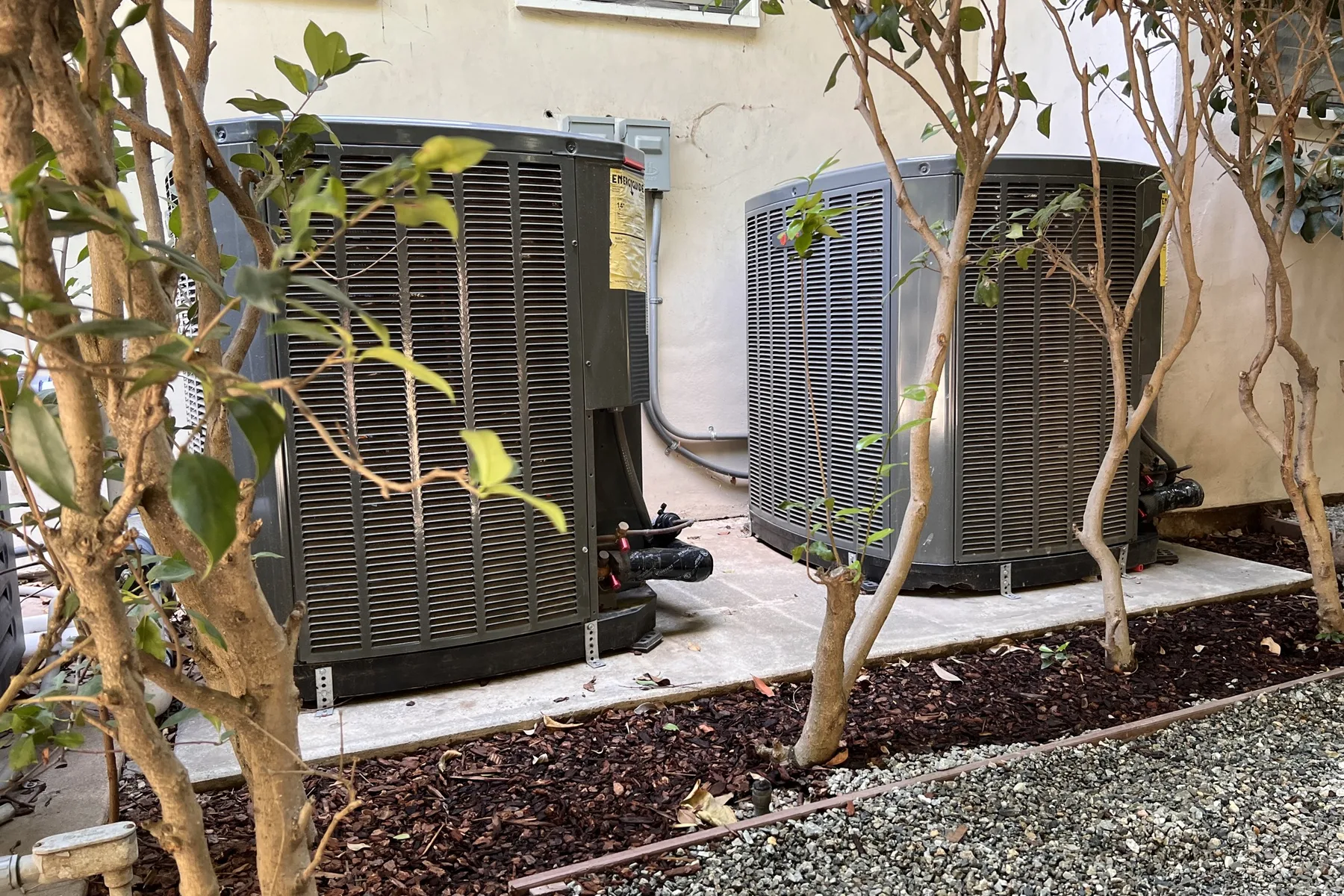 Two outdoor air conditioning units installed against the wall of a home.