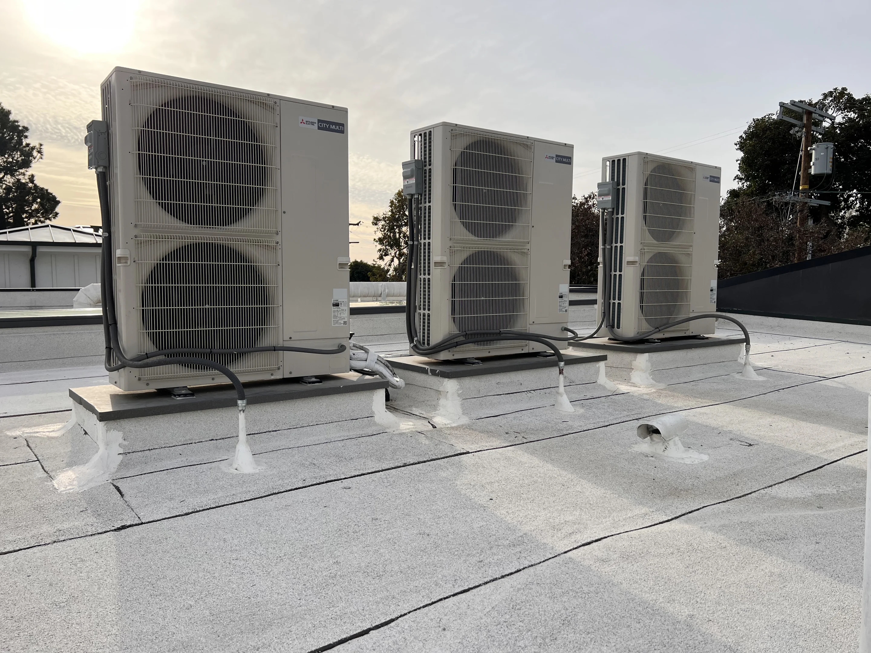 Three new outdoor units on a flat rooftop in evening light.