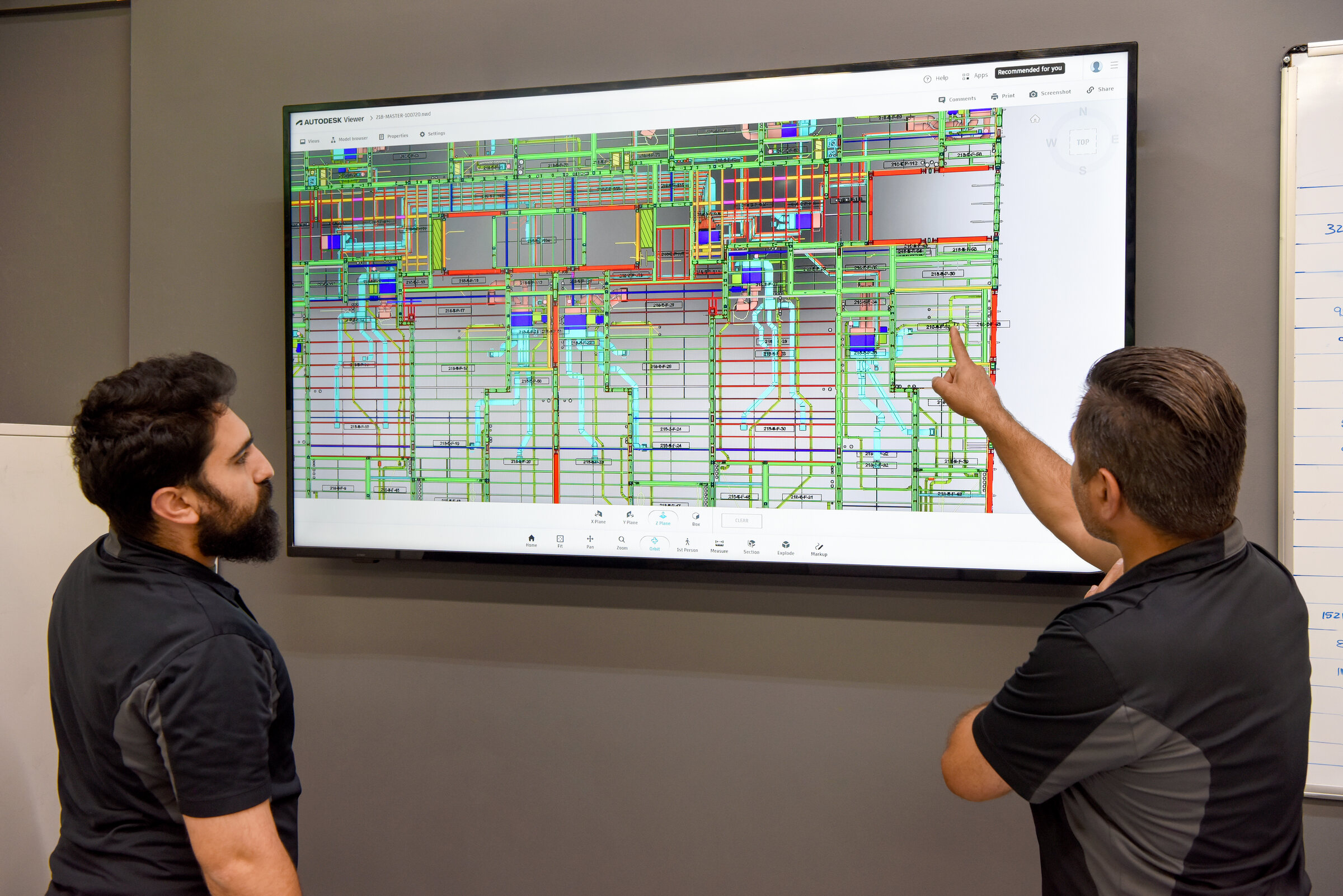 Two Air Plus HVAC team members reviewing a building plan on a wall screen.