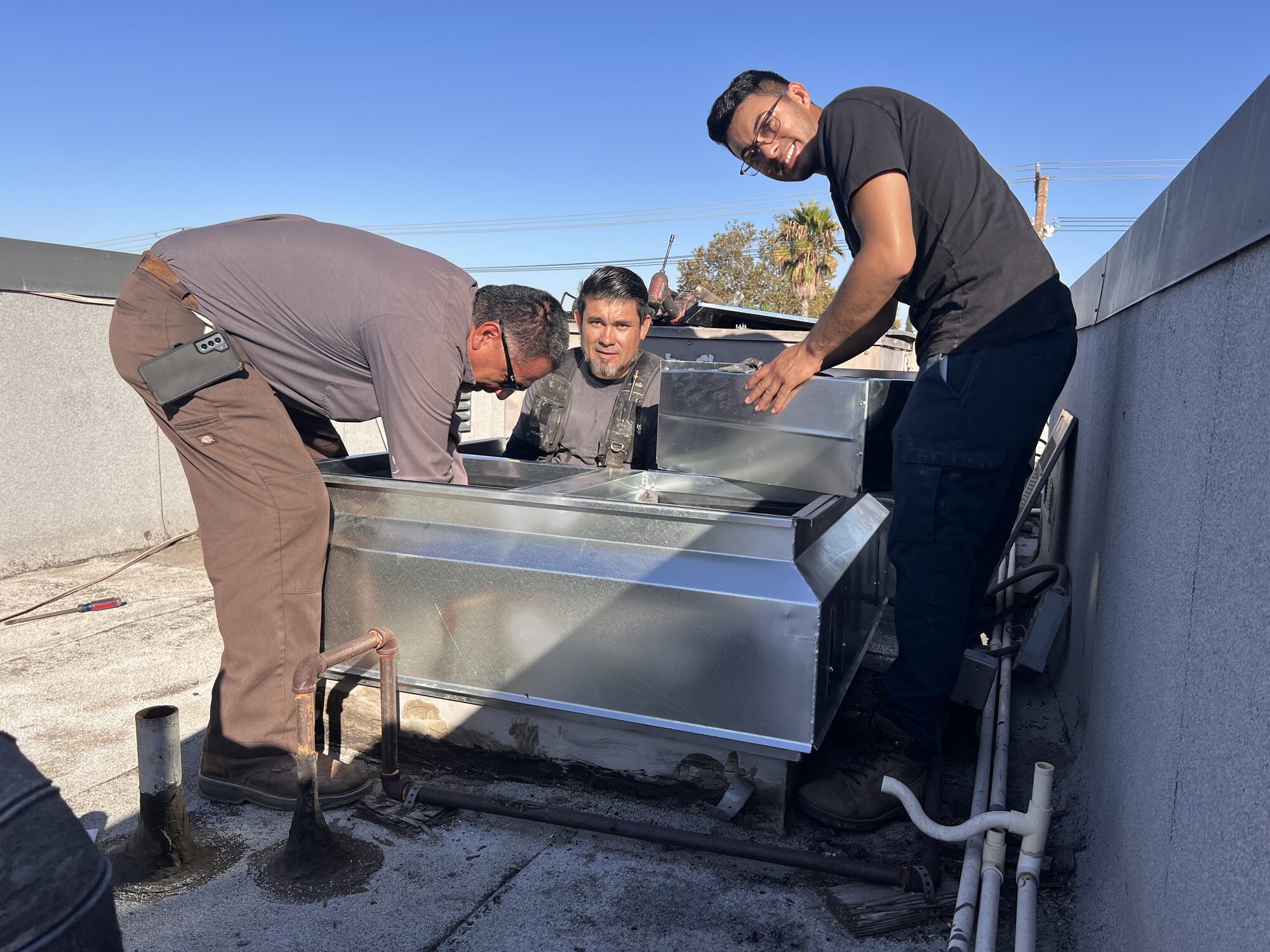 Three Air Plus technicians working around a rooftop air handler.
