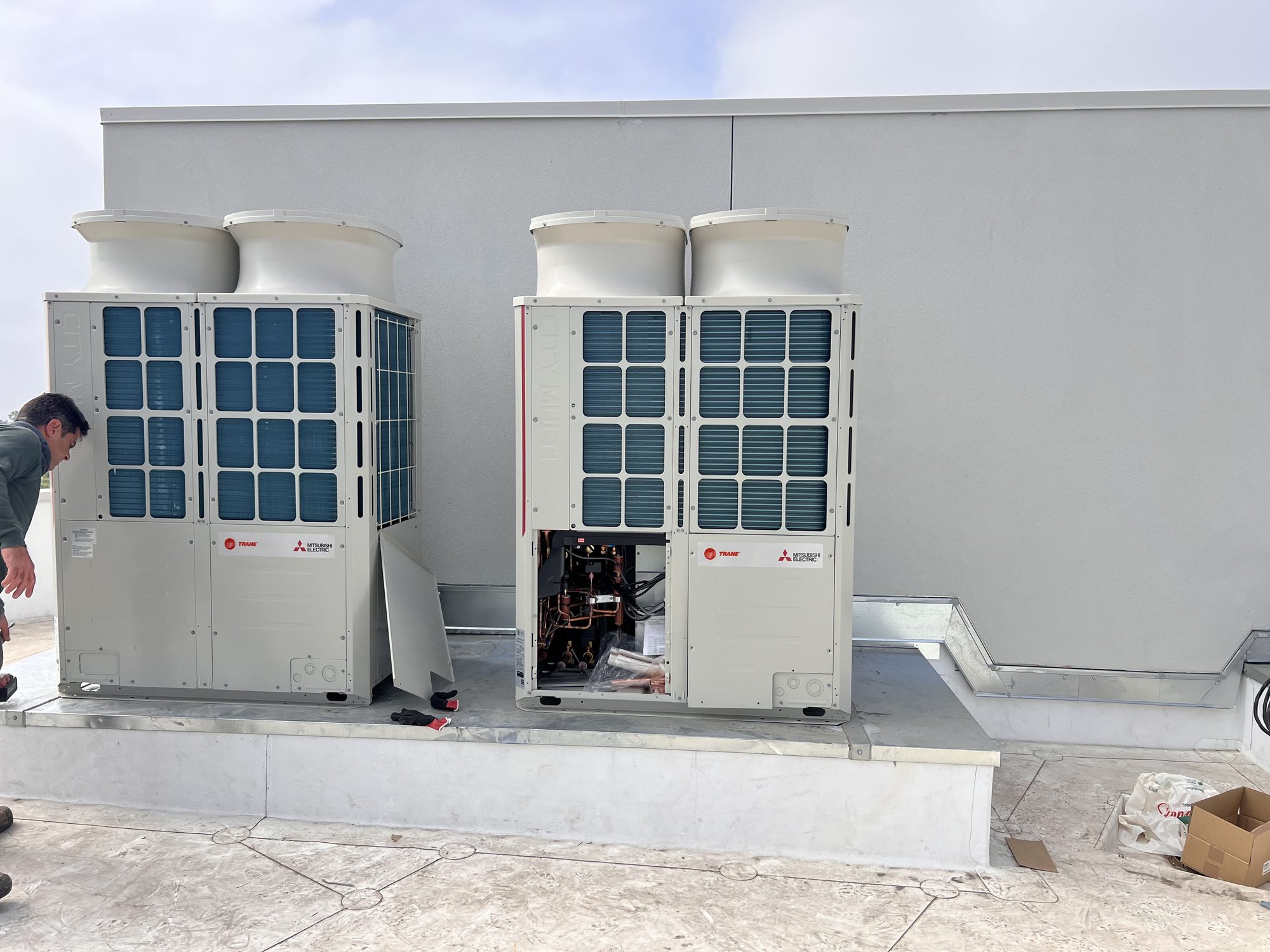 Two outdoor cooling units on a rooftop, one with its service panel open.