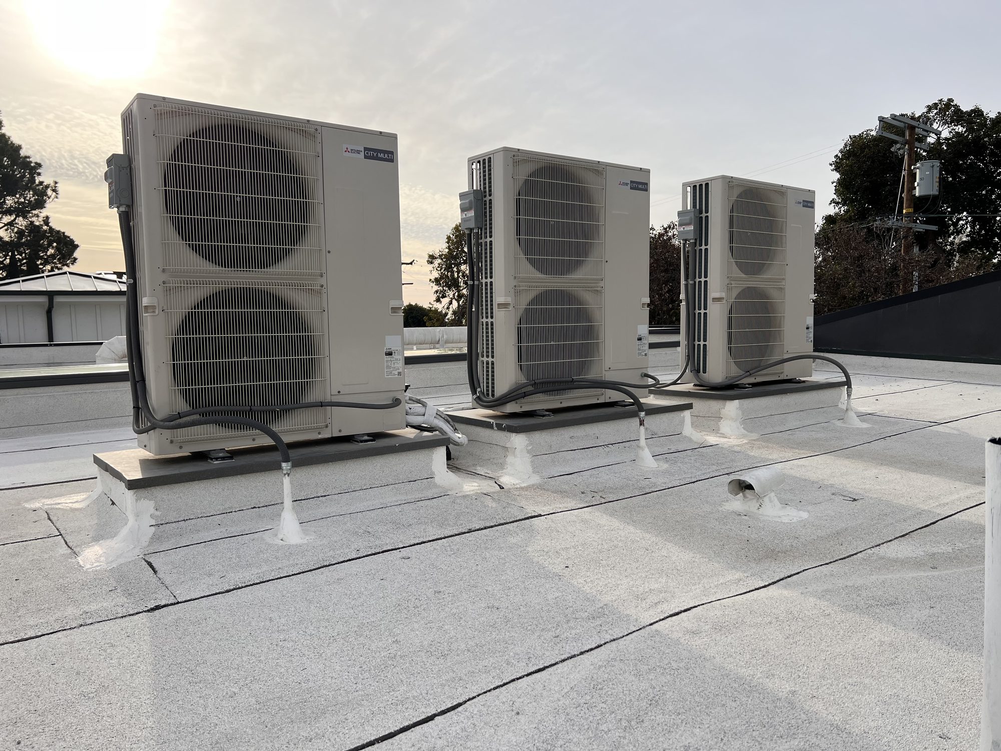 Three outdoor units on a flat roof at sunset.