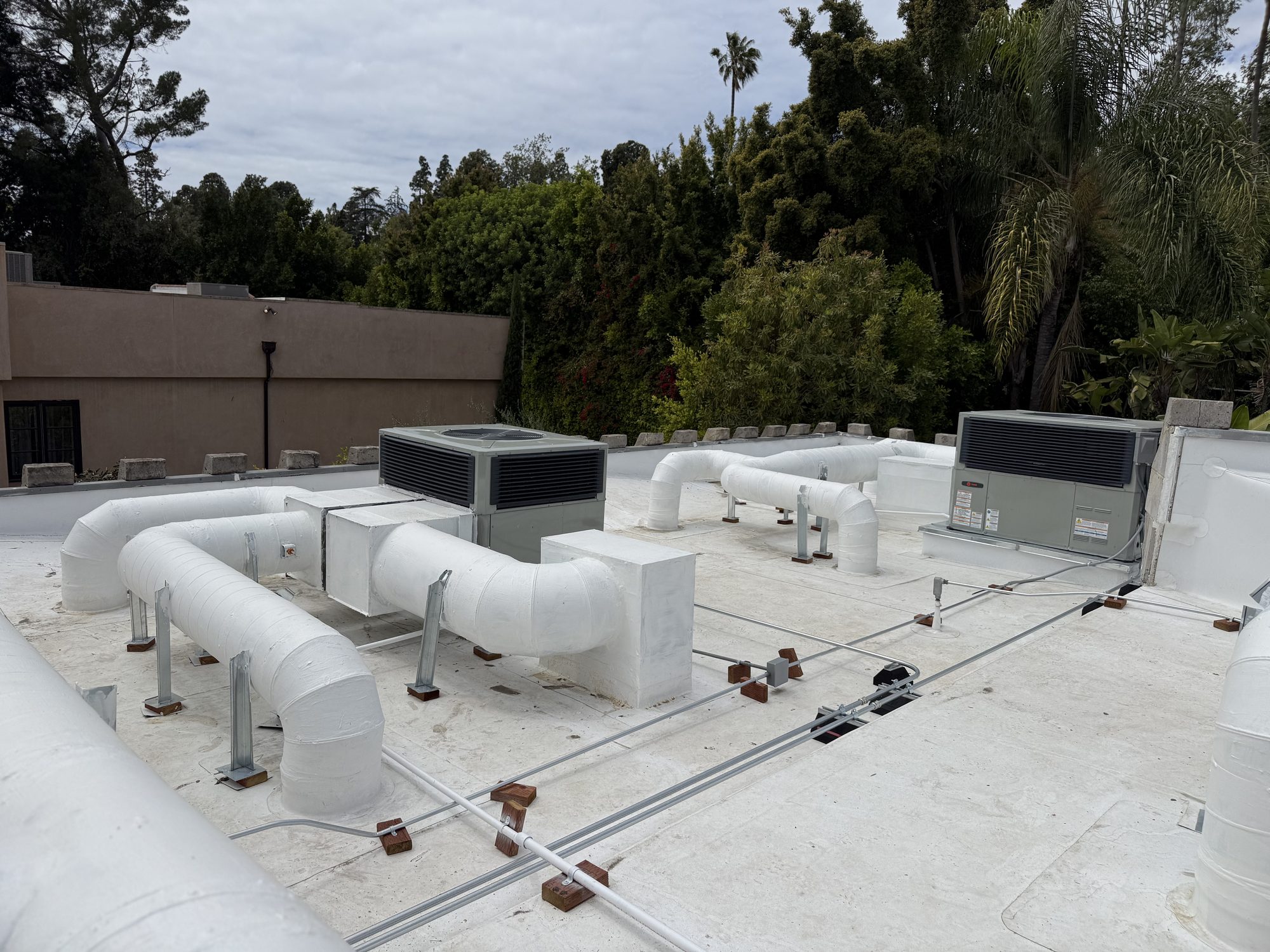 Rooftop heating and cooling units with insulated white ductwork on a flat roof.