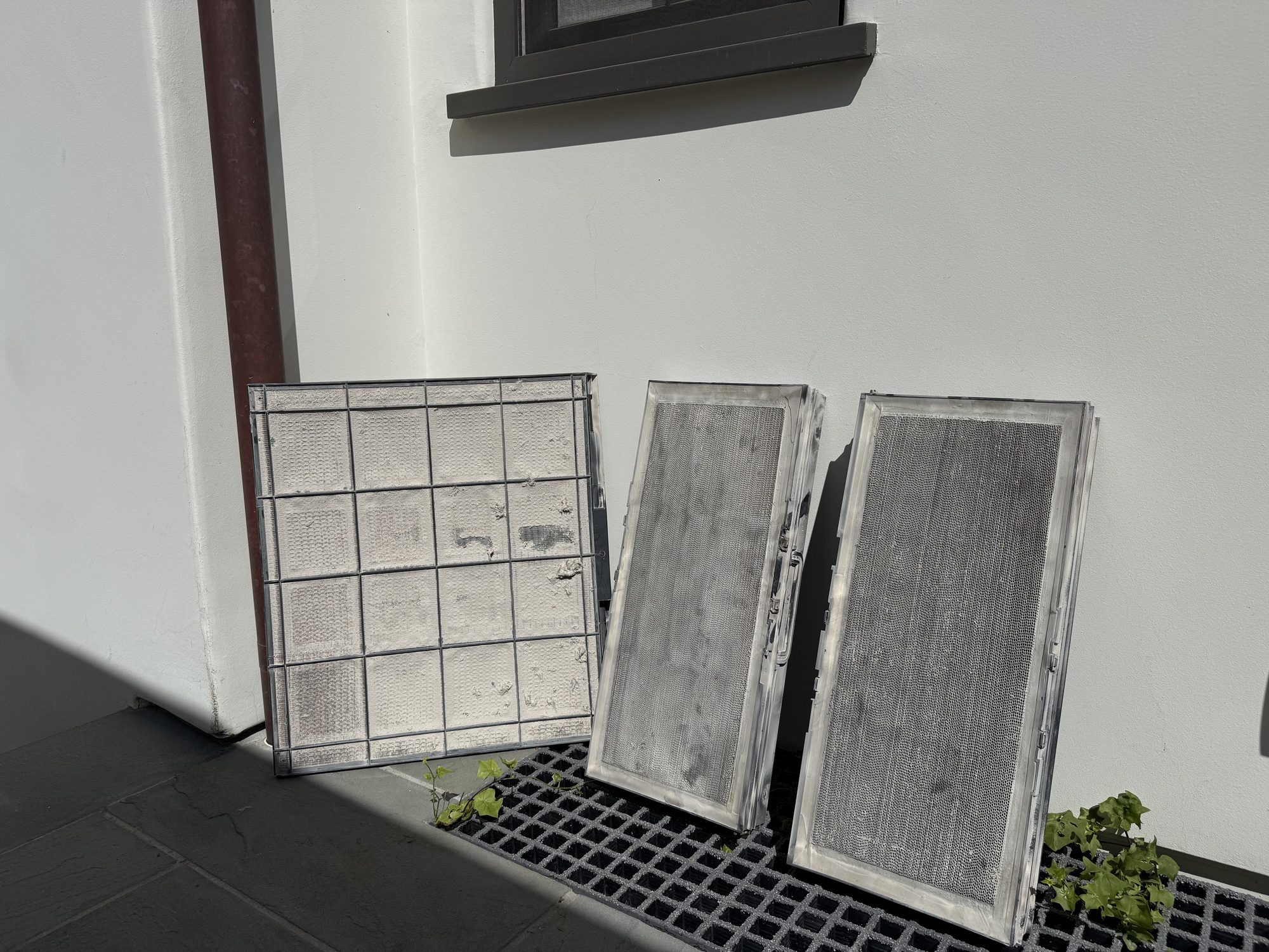Three removed air filters leaning against an outside wall, gray with dust.