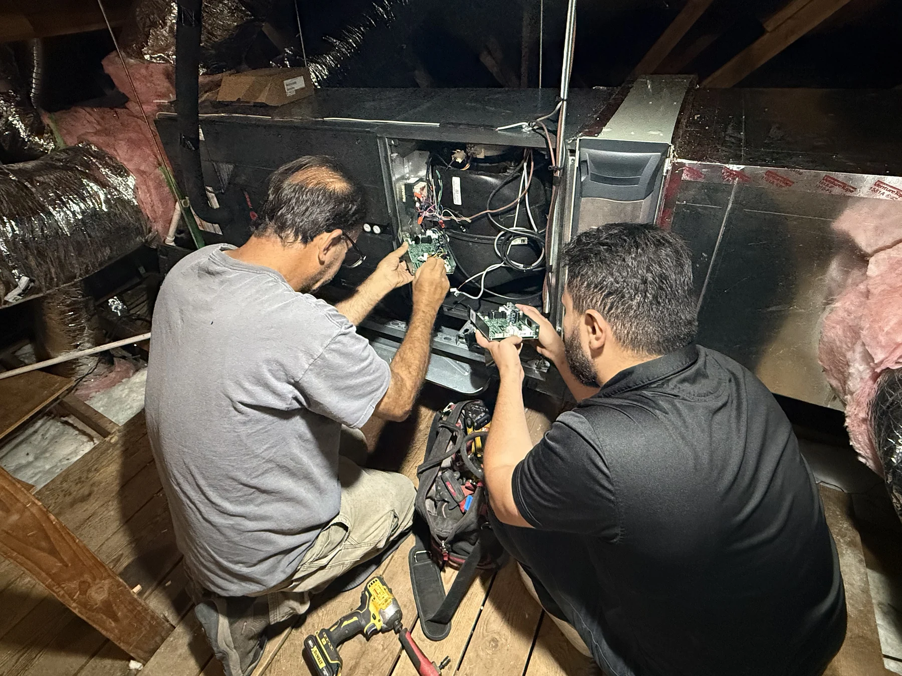 Air Plus technicians working on the control components inside an attic HVAC unit.