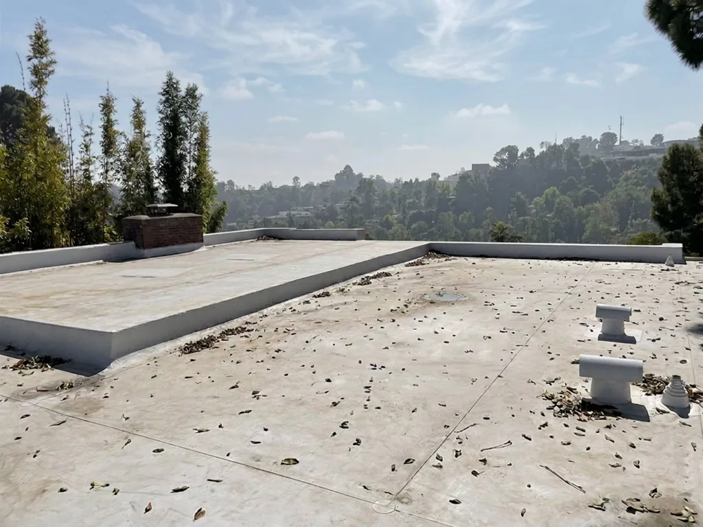Flat roof before ductwork, with a parapet, a brick chimney, and roof vents.
